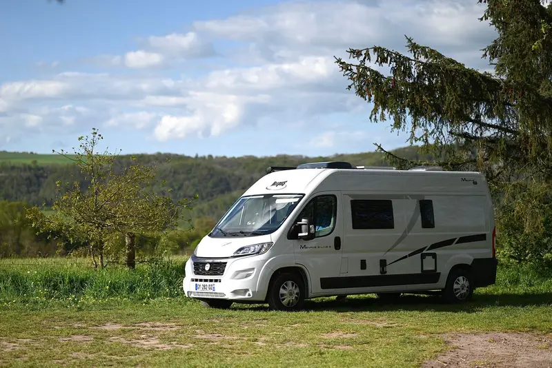 A white motorhome parked on grass in green hilly countryside under a blue sky.